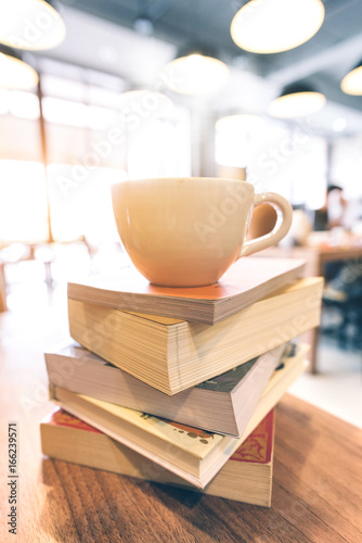A cup of coffee on books stack on the coffee shop table. At the time of university student exams in selective focus.