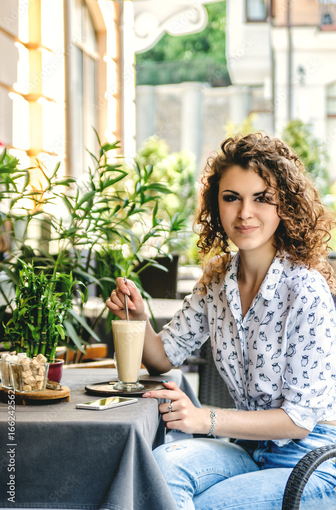 Young beautiful girl in a cafe. She stirs her latte and smiles. Young beautiful girl in a cafe. She stirs her latte and smiles.