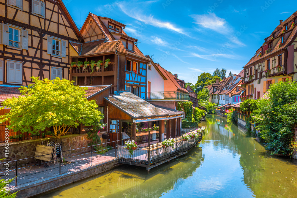 Fototapeta premium Beautiful view of the historic town of Colmar, also known as Little Venice, with tourists taking a boat ride along traditional colorful houses on idyllic river Lauch in summer, Colmar, Alsace, France