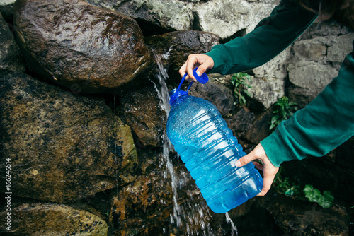 woman hands fill up the bottle from mountain s water source