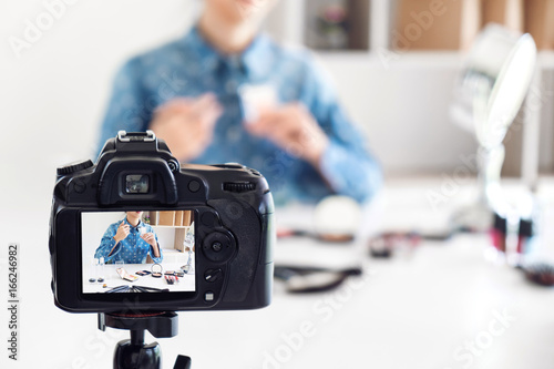 Happy smiling elegant woman or beauty blogger with brush on recording video while review product make up tutorial for theme about video blogging on camera screen