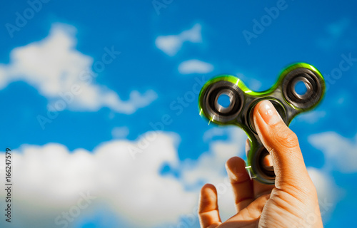 Hand holding popular green fidget spinner toy on sky background. with copy space.