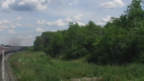 The diesel locomotive smokes and draws a long train. View from the last train car during the turn of the railway to the right.
