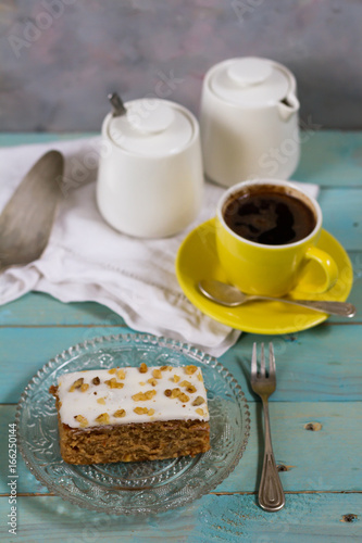 Carrot cake with coffee. Blue wooden table, cristal plate, yellow and orange cup.