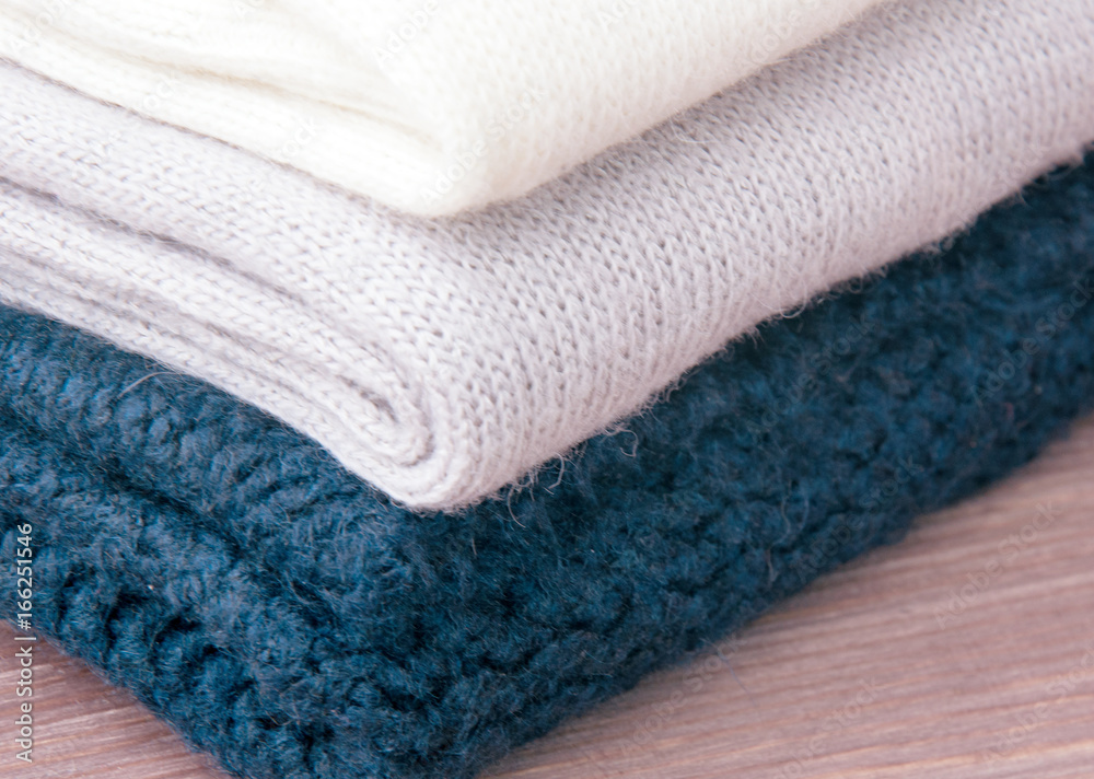 A few stacked warm knitted sweaters, lying on a wooden background. The concept of warm. A few stacked warm knitted sweaters, lying on a wooden background. The concept of warm.