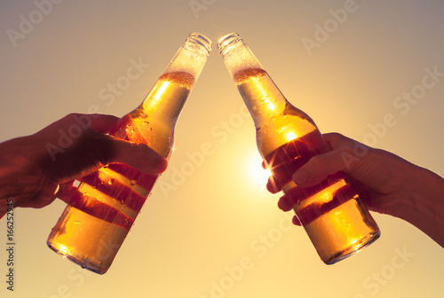 Silhouette of hands toasting bottle of beer outdoors.