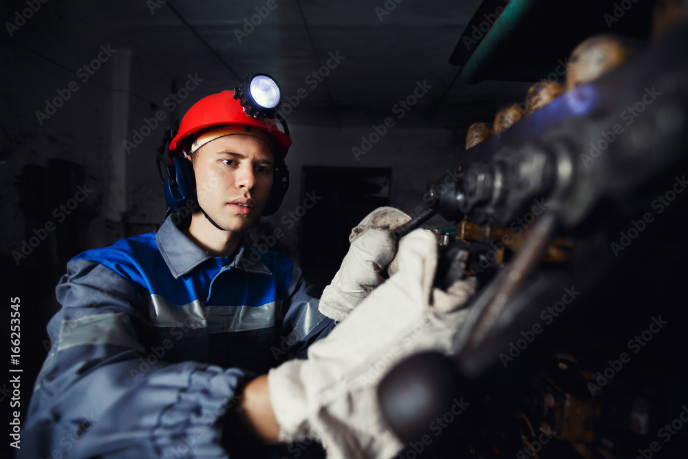 young coal miner is underground in a mine for coal mining in overalls against the backdrop of mining equipment. concept of repair of industrial equipment. young coal miner is underground in a mine for coal mining in overalls against the backdrop of mining equipment. concept of repair of industrial equipment.