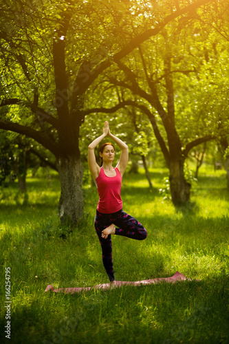 Yoga balance asana training. Woman in garden standing in Vrksasana, exercising yoga in the morning. Toned image.