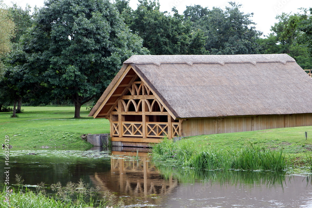 Pretty tudor style wooden framed thatch boathouse in a wood on the edge of a lake or river