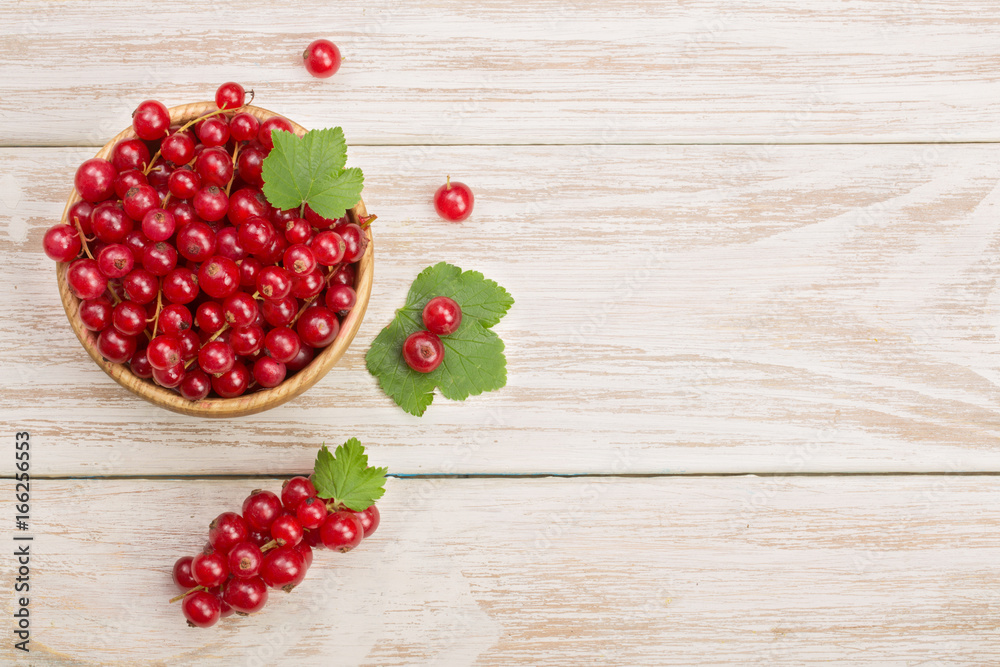 Red currant berries in a wooden bowl with leaf on the white wooden background. Top view Red currant berries in a wooden bowl with leaf on the white wooden background. Top view