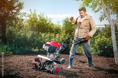 Happy man Farmer plows the land with a cultivator, preparing it for planting vegetables, on a sunny day garden