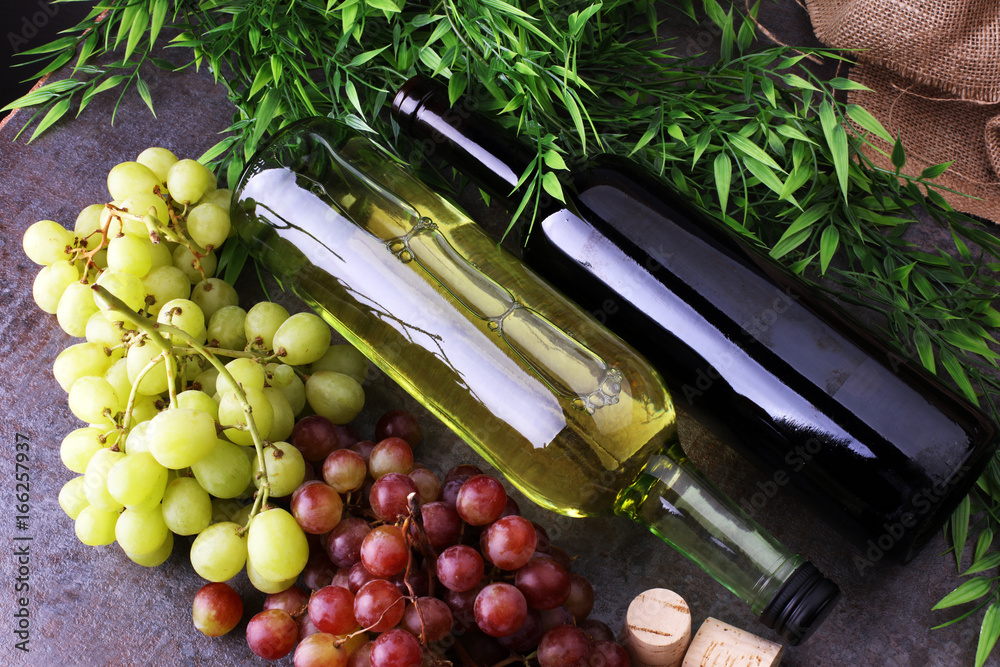 Obraz premium Bottle of white and red wine, grape and corks on wooden table