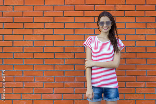Lovely woman wearing striped t-shirt and jeans shorts. Red brick wall background. Empty space