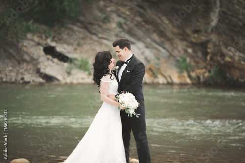 Beautifull wedding couple kissing and embracing near the shore of a mountain river with stones © olegparylyak