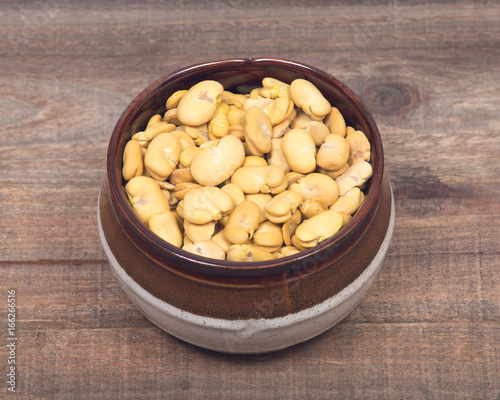 Organic dry broad haba beans in ceramic bowl on wooden vintage background photo