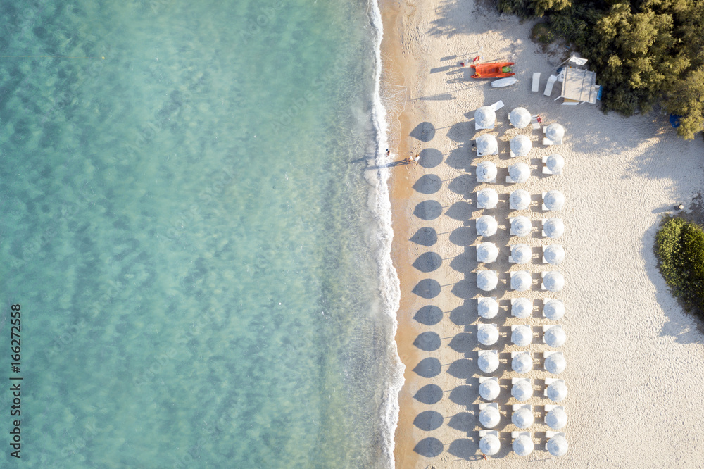 View from above, stunning aerial view of an amazing empty white beach with white beach umbrellas and turquoise clear water during the sunset. Mediterranean sea, Sardinia, Italy.