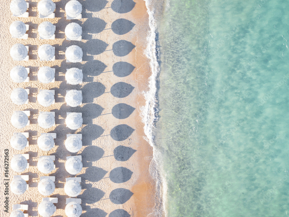 View from above, stunning aerial view of an amazing empty white beach with white beach umbrellas and turquoise clear water during the sunset. Mediterranean sea, Sardinia, Italy.
