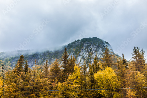 Mountain cliff by highway road with wires in stormy misty and foggy weather in mountain Charlevoix region of Quebec, Canada during autumn