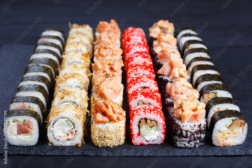 Appetizing multicolored sushi set on black slate, close-up. Traditional japanese food, restaurant serving