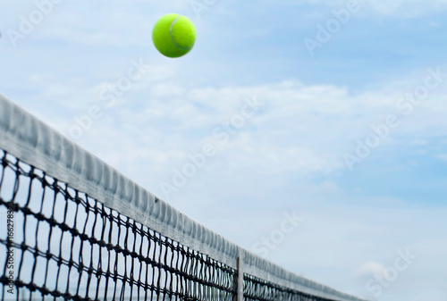 Tennis ball flying over middle net court on background blue sky