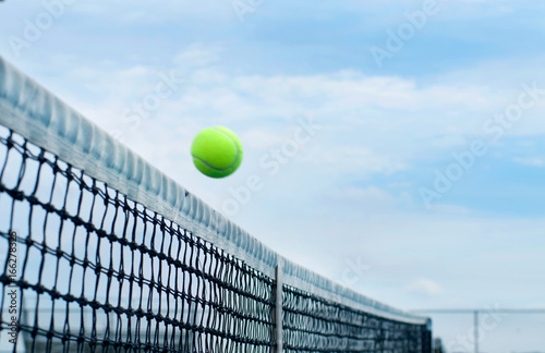Tennis ball flying over middle net court on background blue sky © Dmytro Flisak