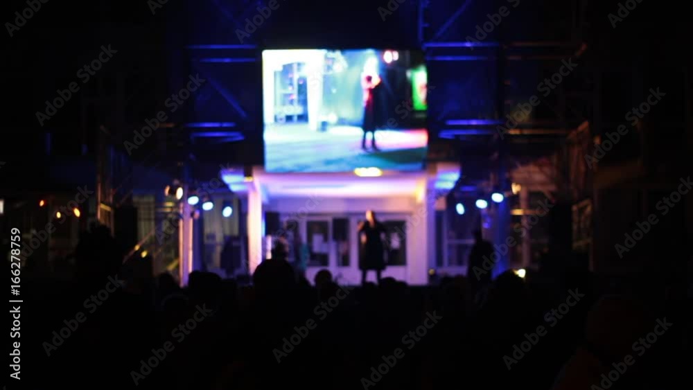 A crowd of people at the concert watches the performance. Artists on stage dance and sing songs. Above Scoreboard for capturing and displaying video. White background instead of green.
