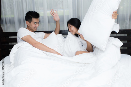 Couple having pillow fight on bed in the morning
