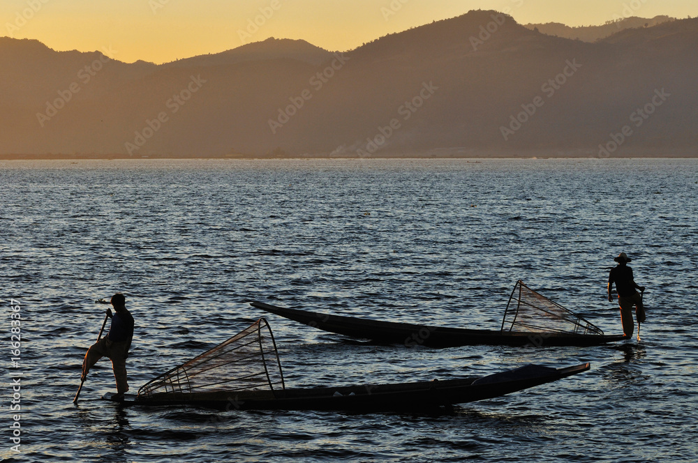 Naklejka premium Silhouette of Burmese fisherman on boat catching fish in traditional way in Inle lake, Myanmar (Burma), Myanmar travel attraction landmark