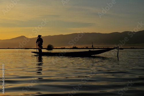 Silhouette of Burmese fisherman on boat catching fish in traditional way in Inle lake, Myanmar (Burma), Myanmar travel attraction landmark