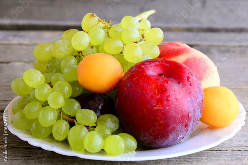 Fresh fruits on a white plate and an old wooden background. Ripe peaches  plums  apricots  grapes branch. Natural healthy food. Summer fruits. Closeup