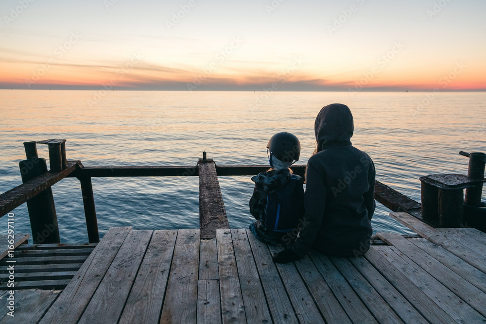 Mother and daughter in sunset jetty lake with orange sun