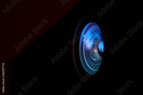 Photo depicts digital projector film presentation. Projector shiny colorful glass lens closeup, macro view, black background.