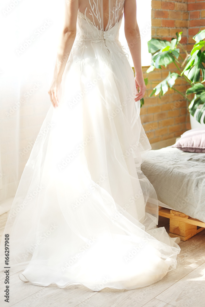 Bride in white dress standing near windows view from the back Bride in white dress standing near windows view from the back