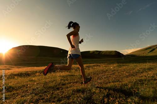 young fitness woman runner running on sunset grassland trail