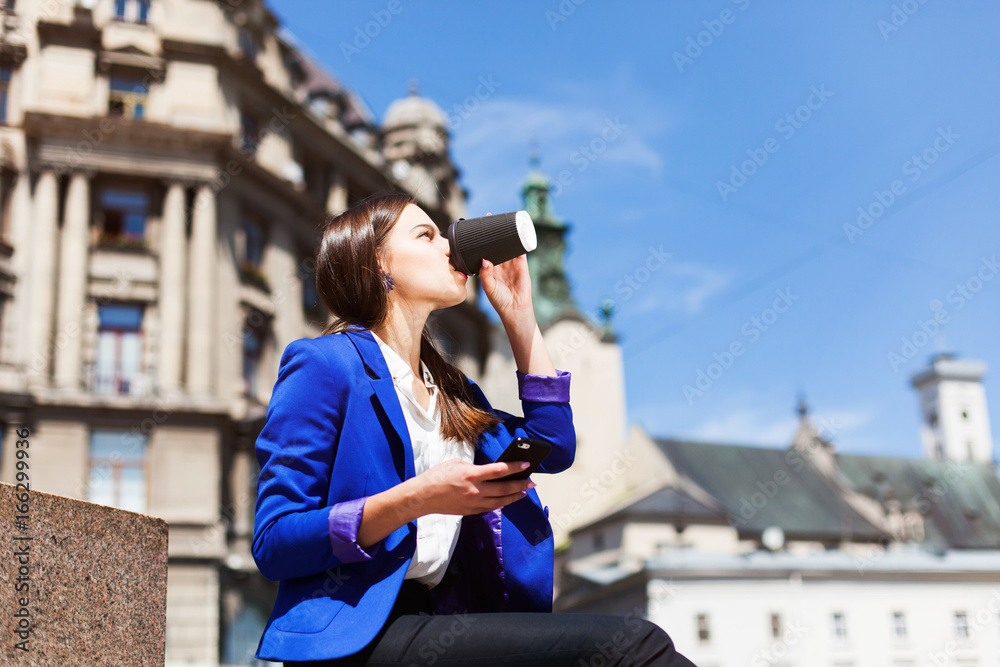Woman checks her phone sitting with cup of coffee on the street Woman checks her phone sitting with cup of coffee on the street