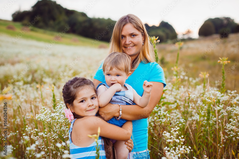Children hug their mom standing on the field with white flowers