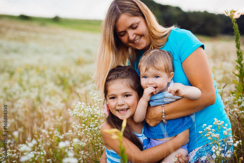Children hug their mom standing on the field with white flowers Children hug their mom standing on the field with white flowers