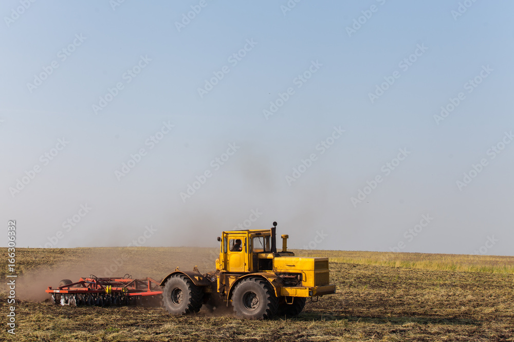 Tractor ploughing a field with a trail of dust behind it Tractor ploughing a field with a trail of dust behind it