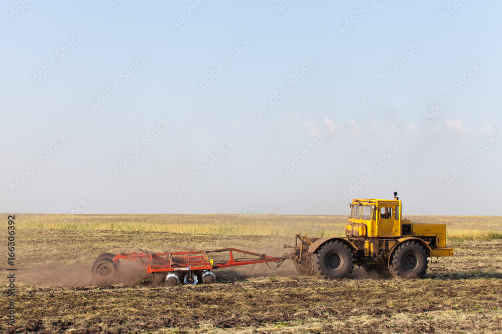 Fototapeta premium Tractor ploughing a field with a trail of dust behind it