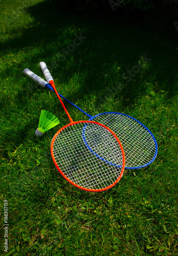 Two badminton racket on the sunny bright grass green fresh background. Photo depicts two colorful shuttlecock rackets in the garden, funny game competition start concept. Closeup, macro view.