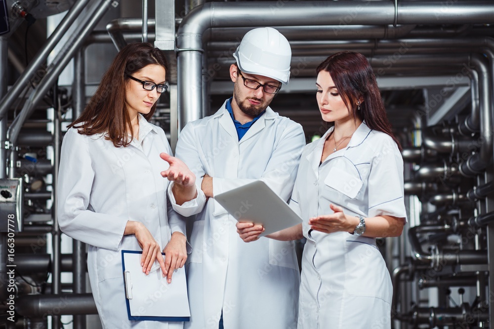 Obraz premium A group of young inspectors in a white coat are conducting an audit at a beer factory.