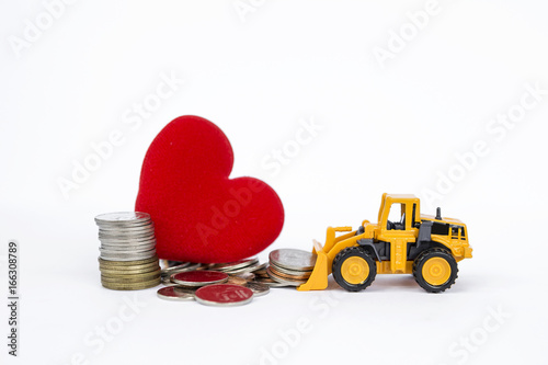 Yellow front loader moving stack of coins with pile of coins and red heart on backgrund, business & financial concept