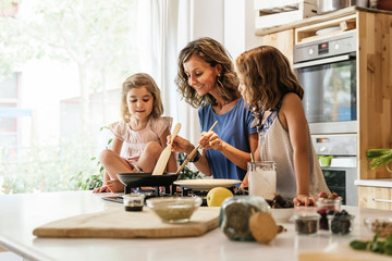 Little sisters cooking with her mother in the kitchen.