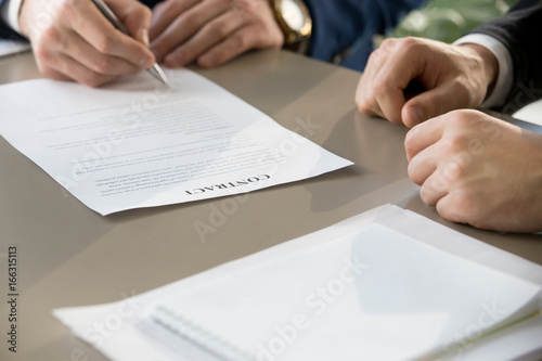 Businessman signing financial contract at formal meeting, male hand putting signature after reaching agreement and making deal, business partnership concept, focus on legal document, close up view