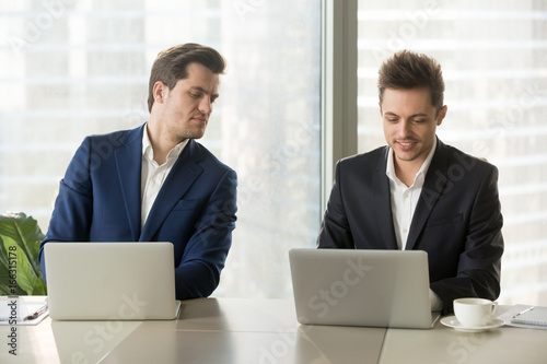 Fototapeta Curious businessman secretly looking at laptop screen of colleague, sneaking pee