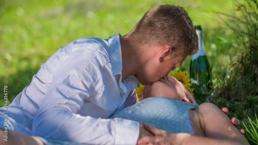 A young couple is kissing on a blanket under a tree and he is also touching her breast. It's summer time. A young couple is kissing on a blanket under a tree and he is also touching her breast. It's summer time.
