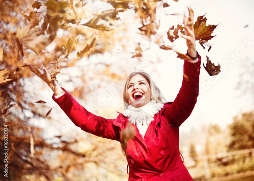 Happy, young woman throwing autumn leaves