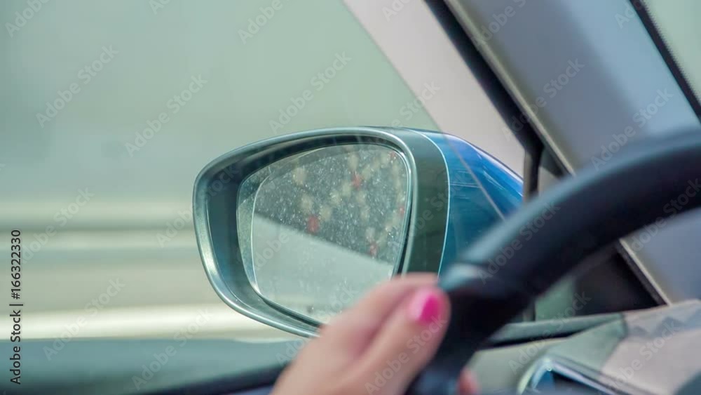 A woman with pink nails is a driver in this car. She is also looking in the side mirror to check the road when driving. A woman with pink nails is a driver in this car. She is also looking in the side mirror to check the road when driving.