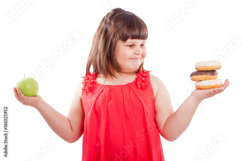 How to teach children to eat healthy food. Girl with food, chooses what to eat donuts or fresh apple, isolated on white background