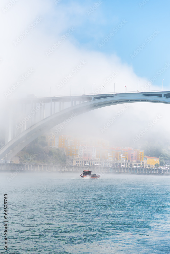 Obraz premium Porto in Portugal, Arrabida bridge, view of the Douro river in the mist, with a traditional boat 